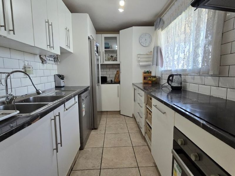 A functional galley-style kitchen featuring white cabinetry, dark countertops, subway tile backsplash, and integrated cooking appliances.