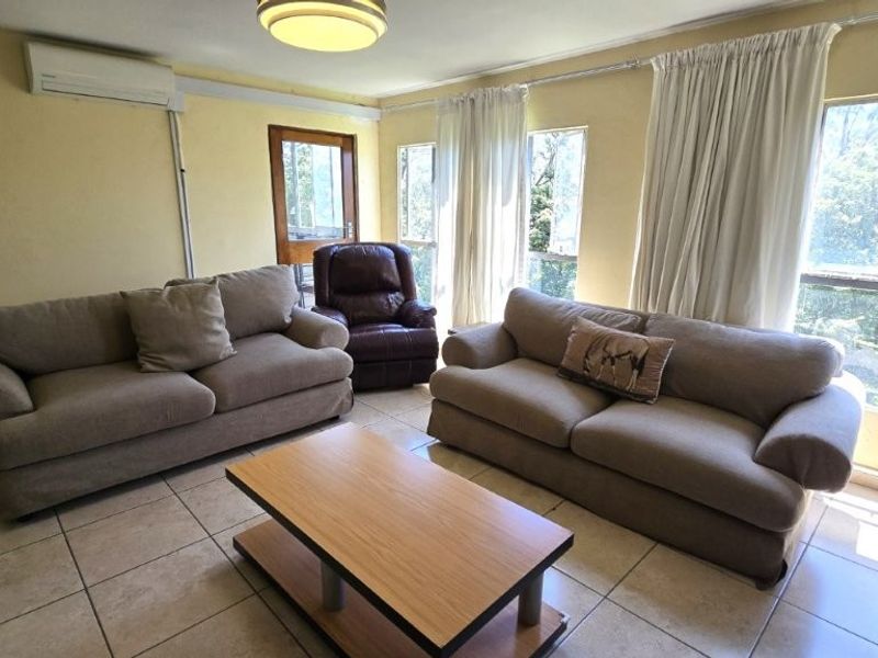 A bright living room featuring tiled flooring, a wall-mounted air conditioning unit, and large windows that provide ample natural light.