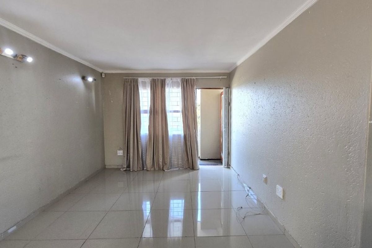An empty, neutrally painted living room featuring tiled flooring, coving, and wall-mounted lighting, offering a blank canvas for interior design.