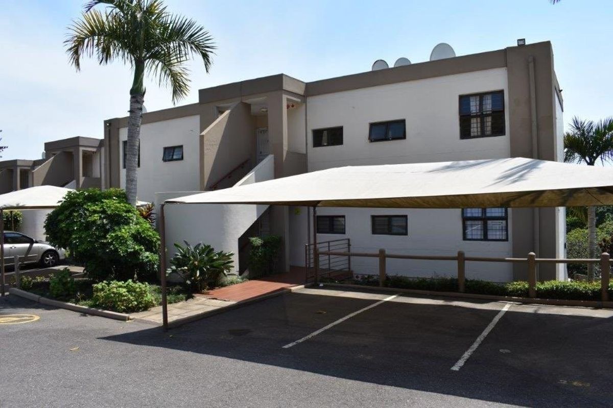Exterior view of a townhouse complex featuring a paved parking area with covered carports and established landscaping.