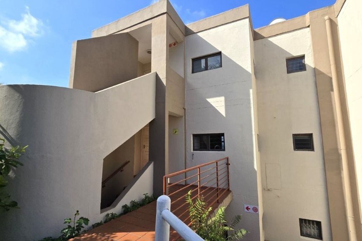 Exterior view of a multi-level townhouse featuring a concrete staircase, tiled walkway, and security windows on the facade.