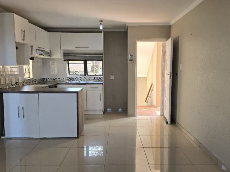 Open plan kitchen and living area featuring white cabinetry, tiled flooring, and direct access to an external staircase.