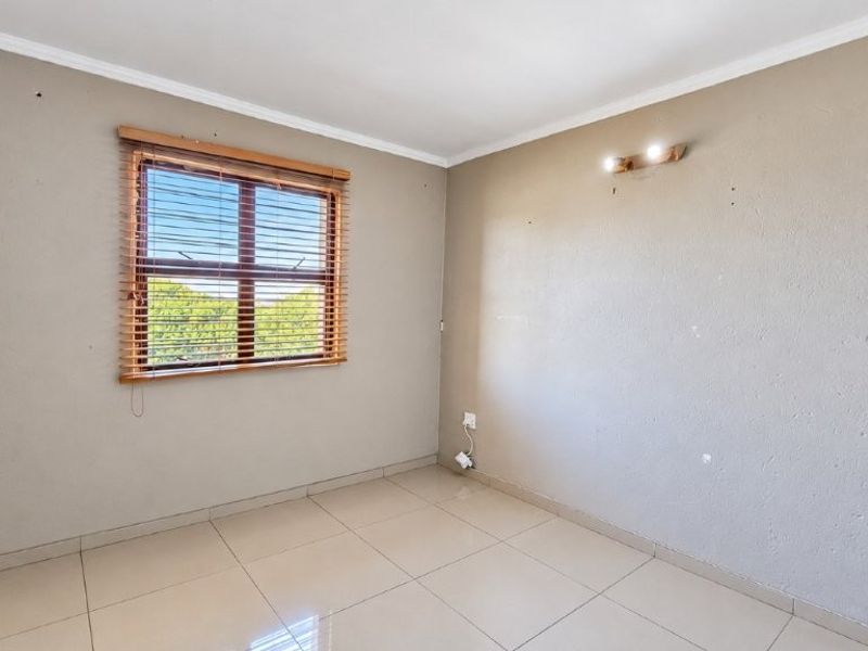 An empty bedroom featuring neutral tiled flooring, a window with wooden blinds, and wall-mounted lighting, ready for personalization.