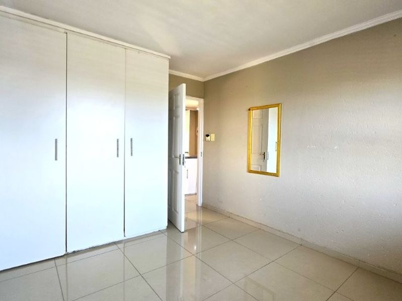 A vacant bedroom featuring neutral tiled flooring and a large white built-in wardrobe, offering a clean canvas for personalization.