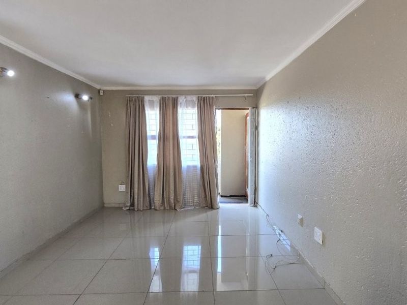 An empty, neutrally painted living room featuring tiled flooring, coving, and wall-mounted lighting, offering a blank canvas for interior design.