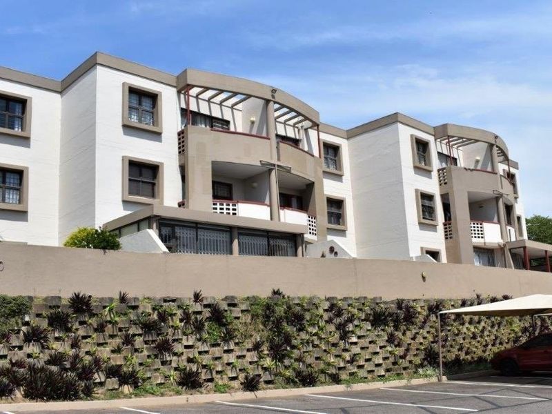 Exterior view of a multi-story townhouse complex featuring private balconies, secure parking, and a landscaped retaining wall.
