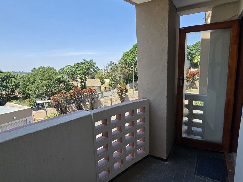 A covered balcony featuring a decorative breeze block balustrade, tiled flooring, and a timber-framed glass door with views over the surrounding neighborhood.