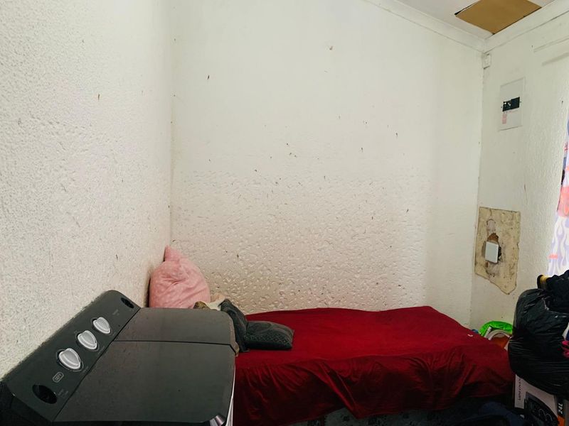 A bedroom space requiring significant renovation, featuring damaged wall plaster, stained surfaces, and a damaged ceiling panel.