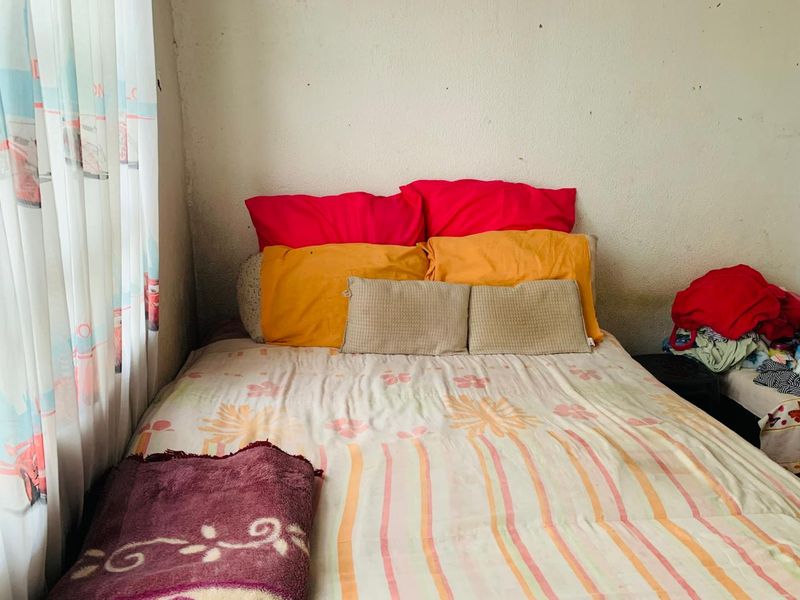 A bedroom featuring a bed against a wall with visible surface wear and staining, requiring cosmetic updates to improve the overall finish.