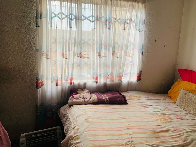 A bedroom featuring a window with a security gate, showing signs of wear on the wall surfaces.