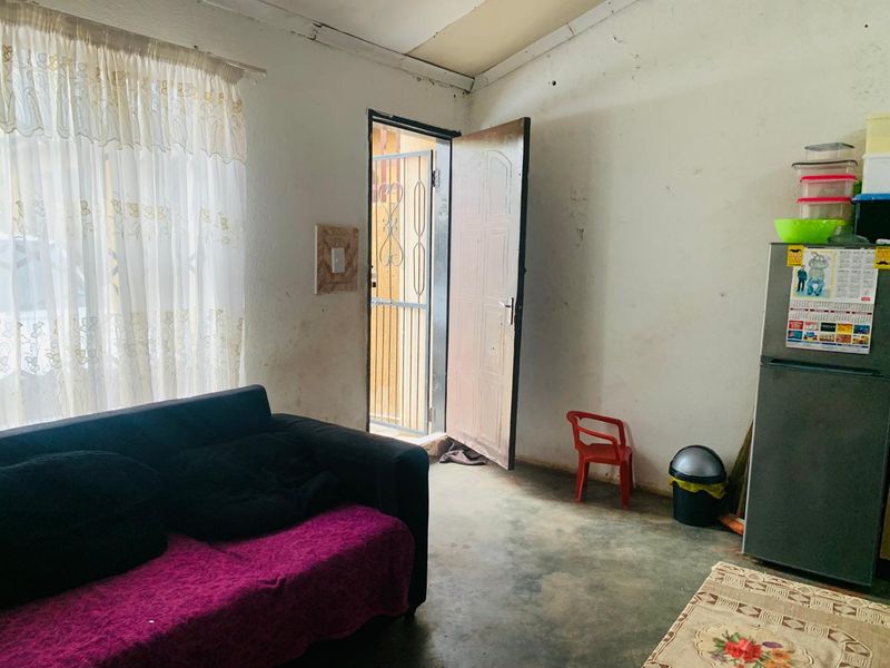 A living area featuring a security gate entrance, plain walls requiring maintenance, and concrete flooring.