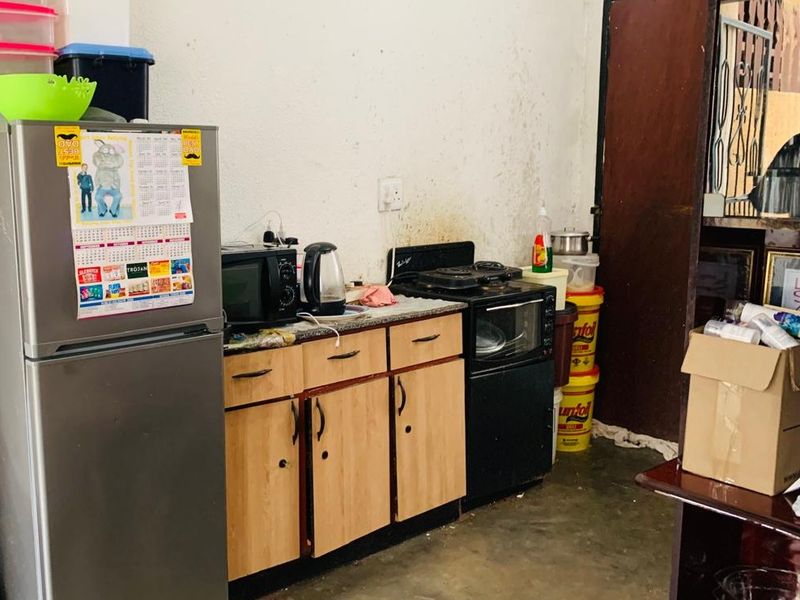 A compact kitchen area featuring basic cabinetry, a countertop, and a freestanding stove, requiring cosmetic updates and wall repairs.
