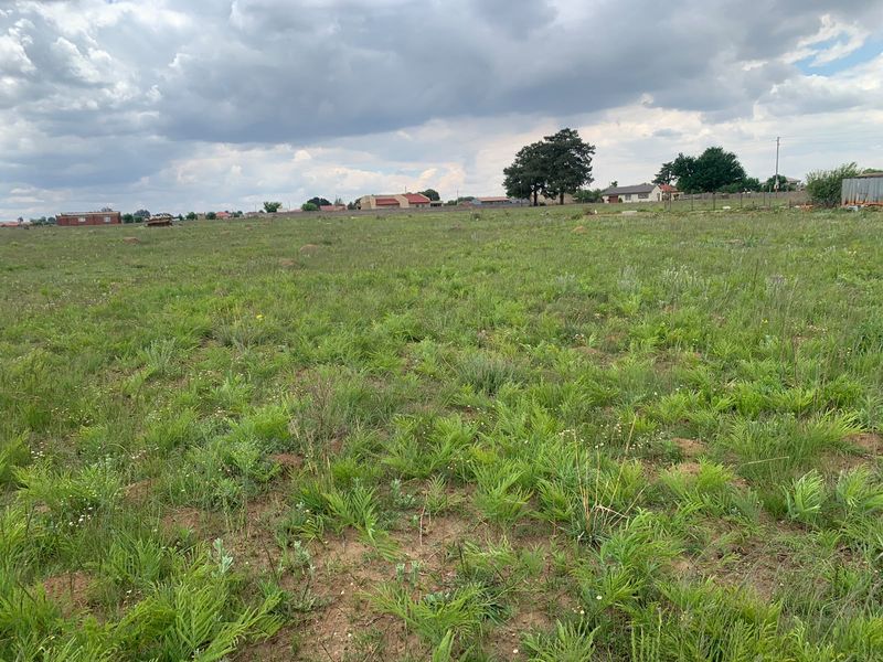A wide-angle view of a vacant residential plot featuring natural grassland and surrounding neighborhood views.