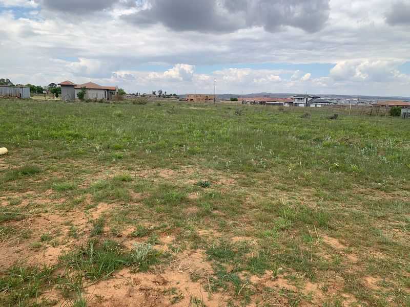 A vacant residential plot of land featuring natural grassland, suitable for future development in a developing neighborhood.