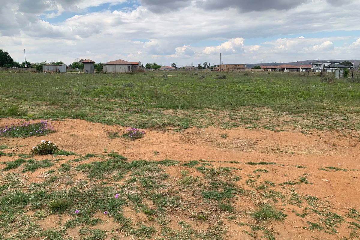 A wide-angle view of a vacant residential plot featuring natural grassland and open terrain in a developing neighborhood.