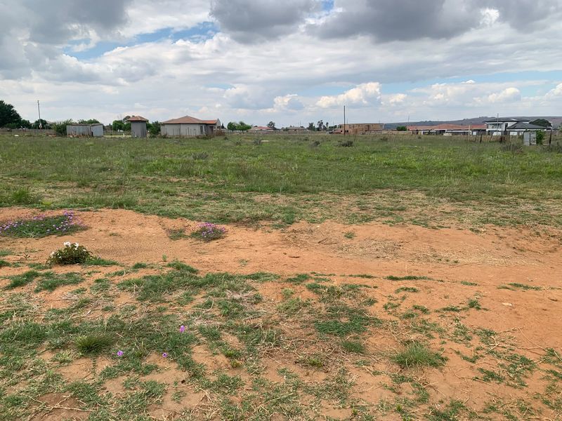 A wide-angle view of a vacant residential plot featuring natural grassland and open terrain in a developing neighborhood.