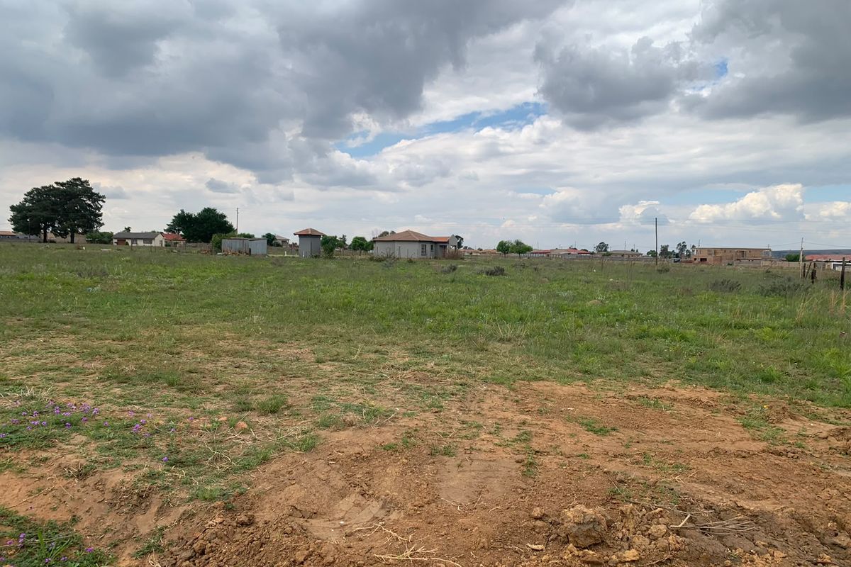 A wide-angle view of a vacant residential plot featuring open grassland and surrounding neighborhood infrastructure.