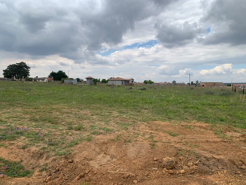 A wide-angle view of a vacant residential plot featuring open grassland and surrounding neighborhood infrastructure.