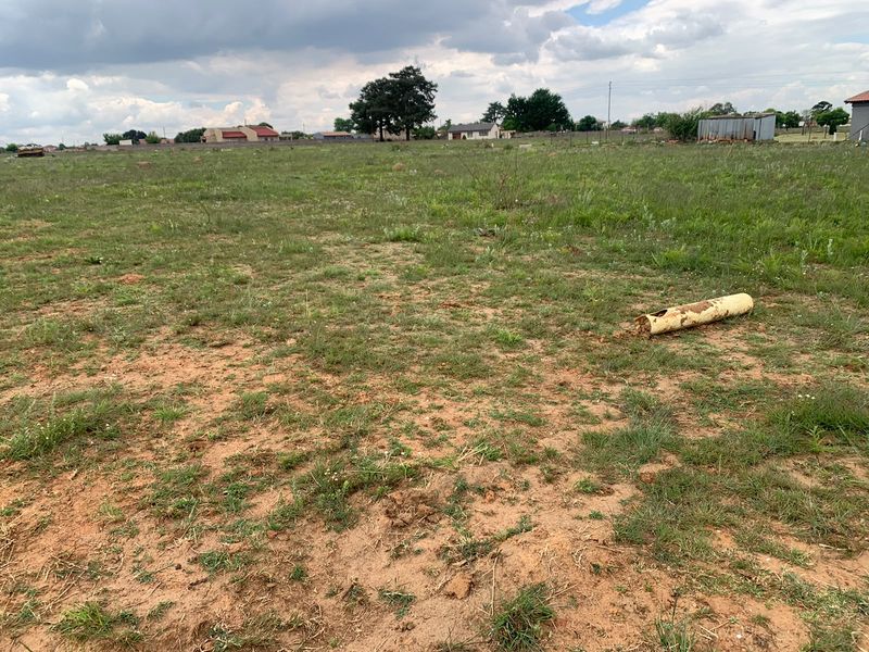 A vacant residential plot featuring open grassland and perimeter fencing, suitable for future development.