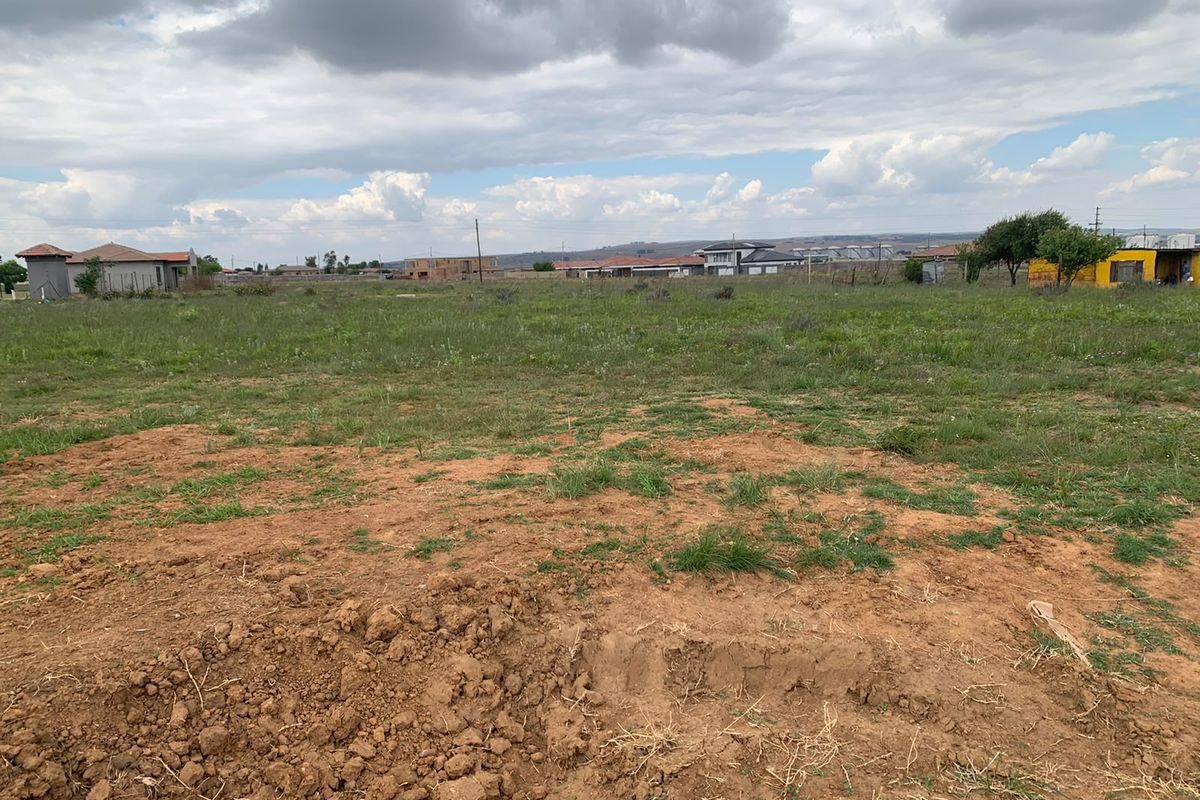 A view of a vacant residential plot featuring open grassland and surrounding neighborhood development.