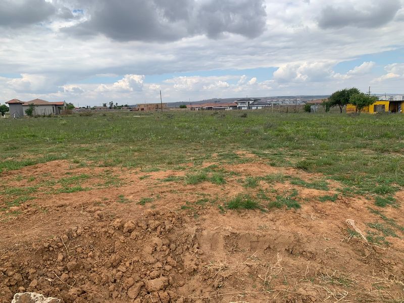 A view of a vacant residential plot featuring open grassland and surrounding neighborhood development.