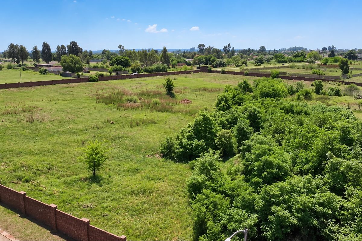An aerial view of a large, level residential vacant plot enclosed by a brick perimeter wall with established greenery.