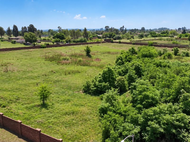 An aerial view of a large, level residential vacant plot enclosed by a brick perimeter wall with established greenery.
