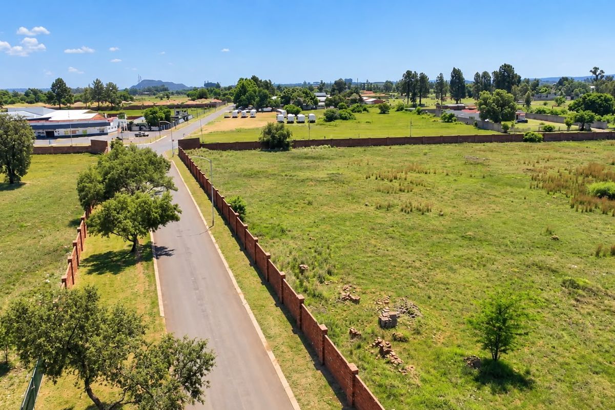 Aerial view of a vacant residential plot featuring a brick boundary wall and adjacent paved road access in a suburban setting.