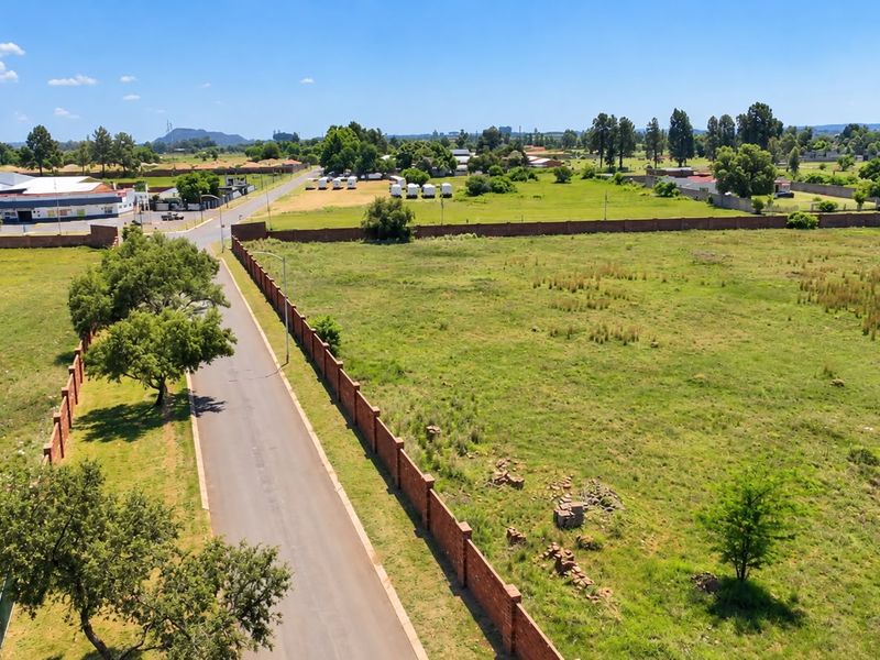 Aerial view of a vacant residential plot featuring a brick boundary wall and adjacent paved road access in a suburban setting.