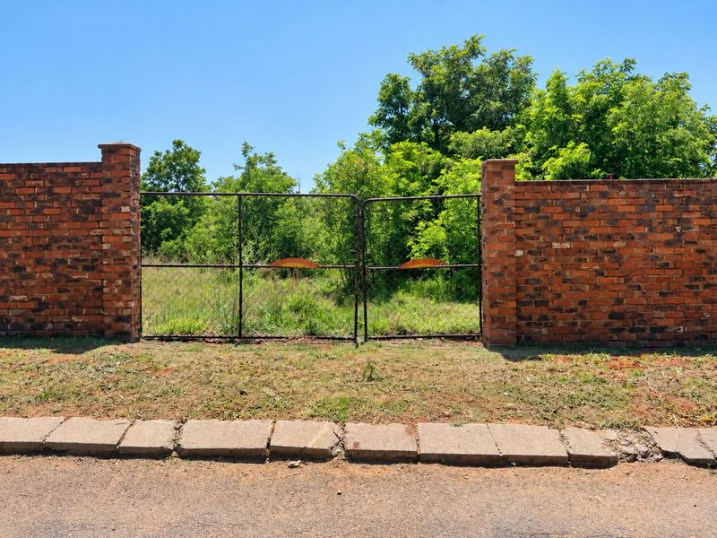 A vacant residential plot featuring a brick boundary wall and metal gate entrance from the street.