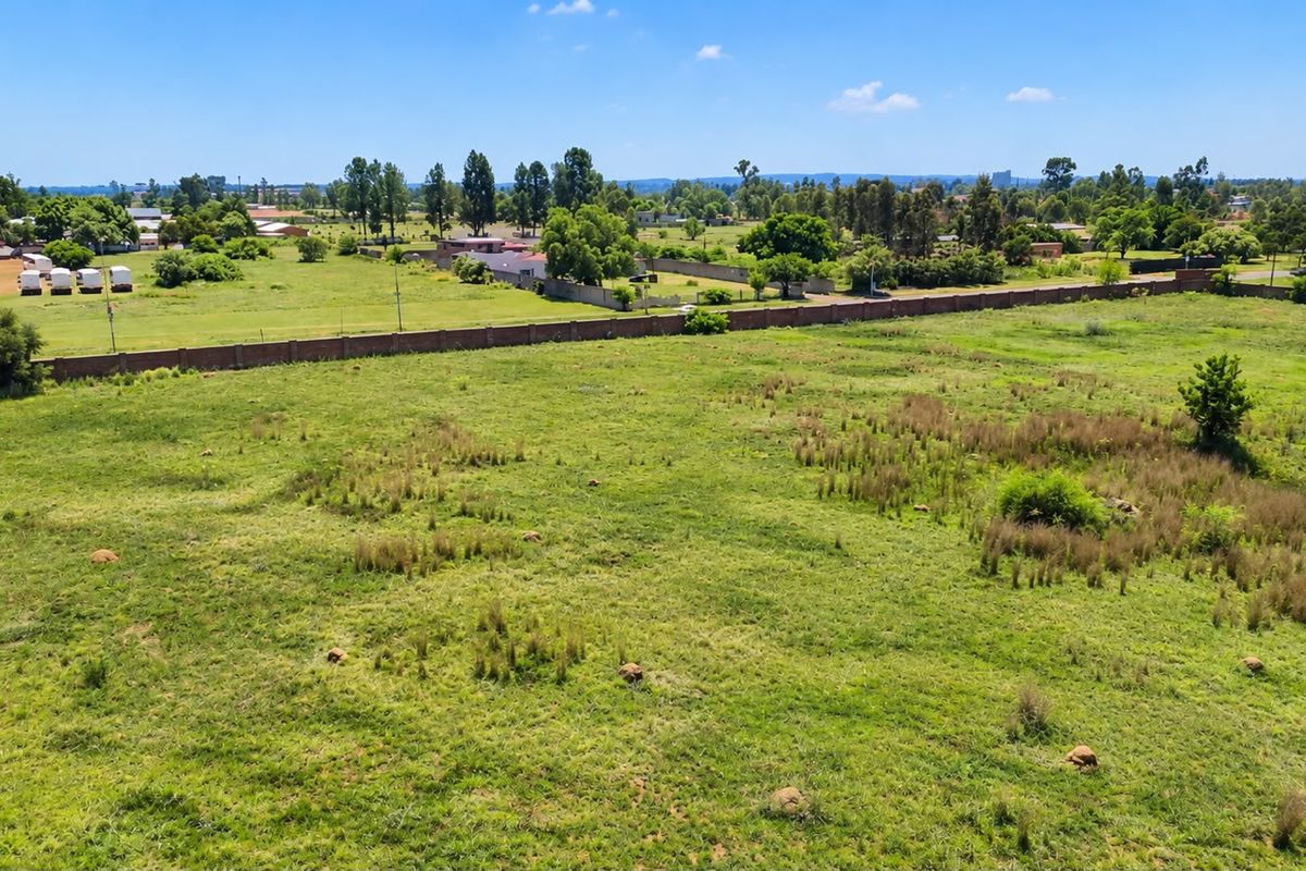 An aerial view of a large, vacant residential plot featuring open grassland and a perimeter boundary wall in a suburban setting.