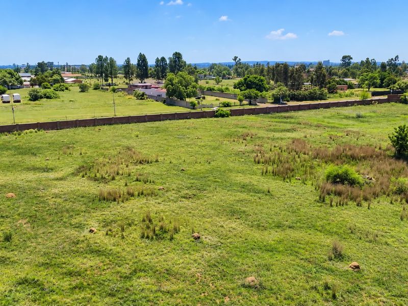 An aerial view of a large, vacant residential plot featuring open grassland and a perimeter boundary wall in a suburban setting.