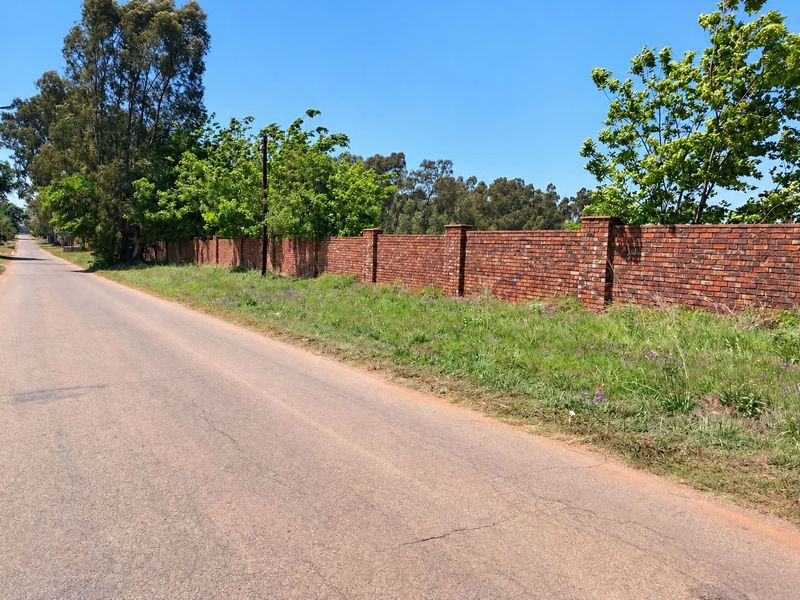 Street view of the property featuring a long, well-maintained brick boundary wall along the paved road.