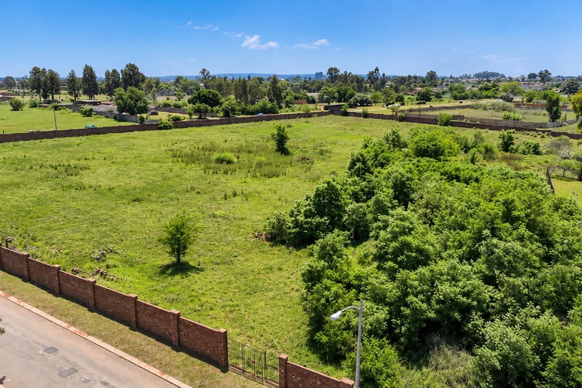 An aerial view of a large, vacant residential plot featuring established trees, a brick perimeter wall, and street access.