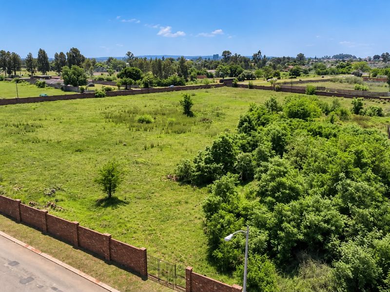 An aerial view of a large, vacant residential plot featuring established trees, a brick perimeter wall, and street access.