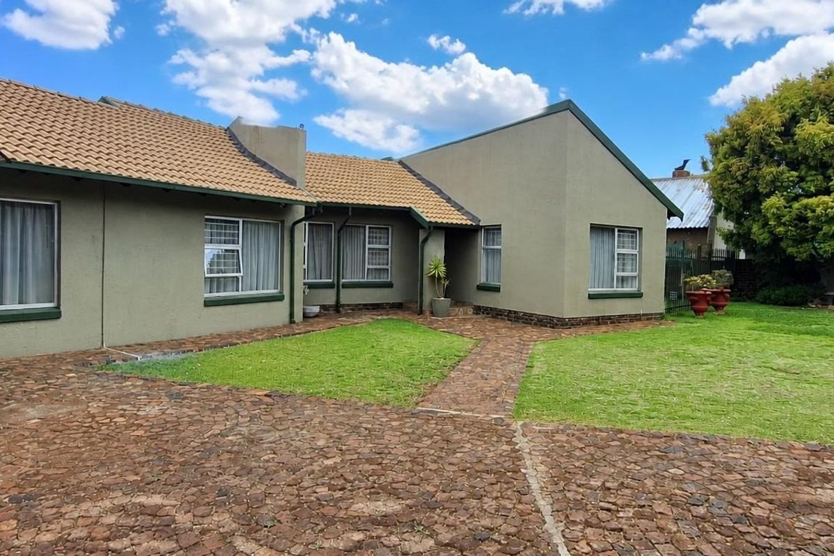 A well-maintained rear exterior view of the house featuring a paved courtyard, manicured lawn, and tiled roof.