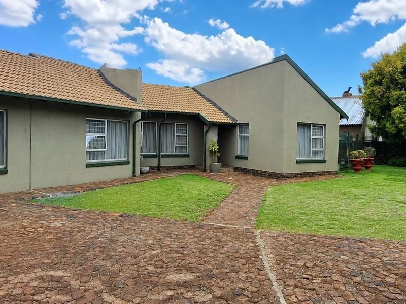 A well-maintained rear exterior view of the house featuring a paved courtyard, manicured lawn, and tiled roof.