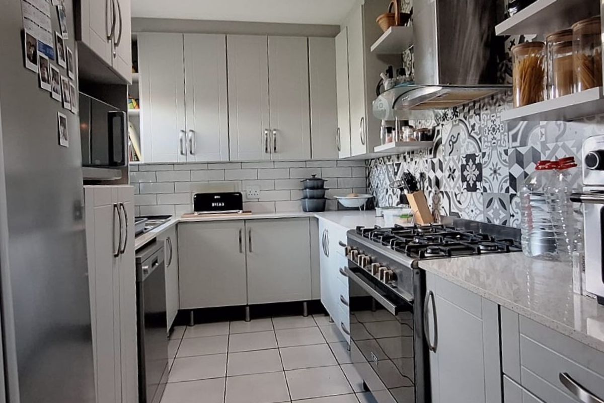 A well-appointed kitchen featuring modern grey cabinetry, stone countertops, a gas stove with extractor fan, and a stylish patterned tile backsplash.
