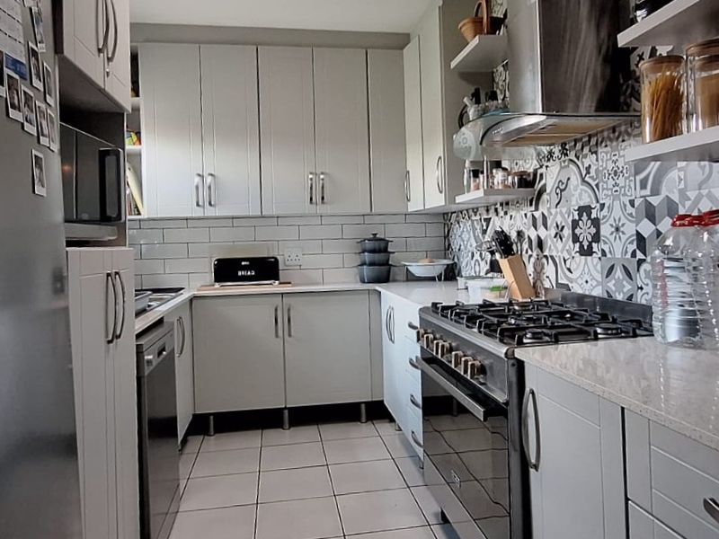 A well-appointed kitchen featuring modern grey cabinetry, stone countertops, a gas stove with extractor fan, and a stylish patterned tile backsplash.