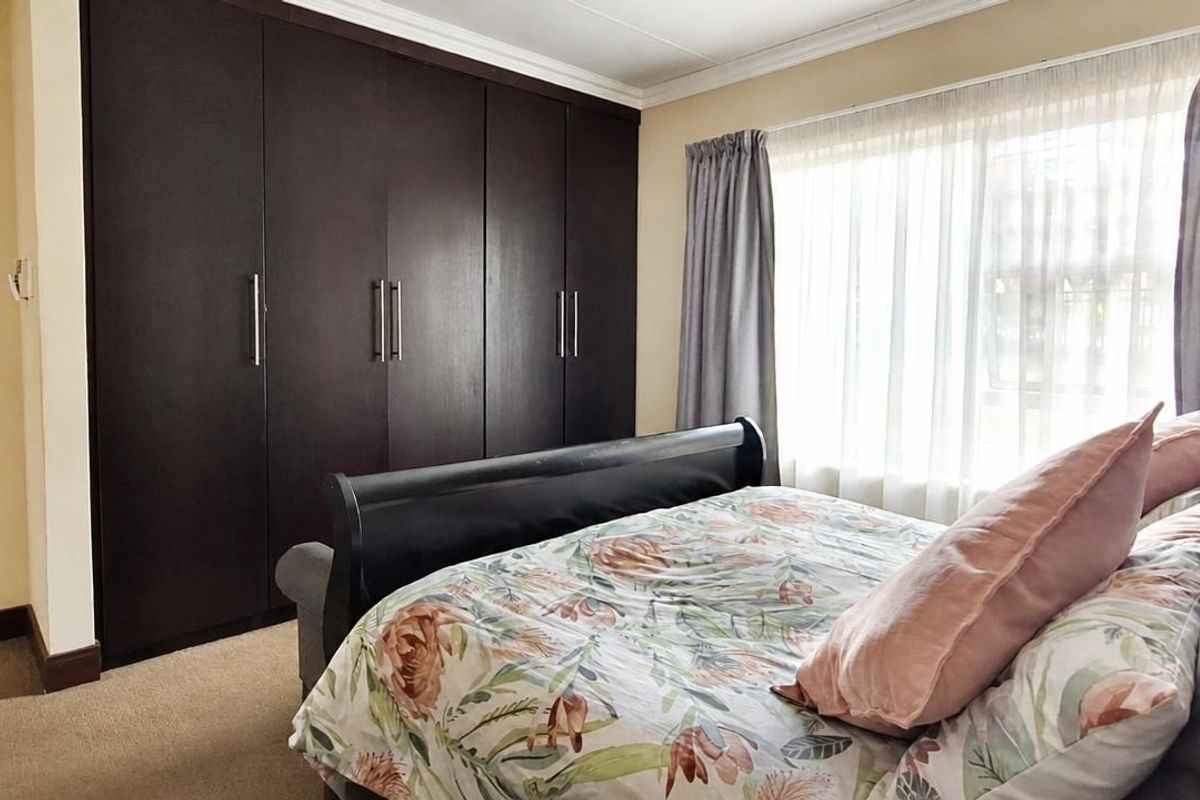 A well-maintained bedroom featuring dark wood built-in cupboards, neutral carpeting, and a coved ceiling, offering a comfortable and functional living space.