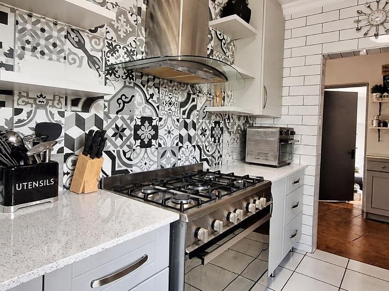Modern kitchen featuring a gas stove, extractor fan, quartz countertops, and a striking patterned tile backsplash, with an adjacent scullery area.