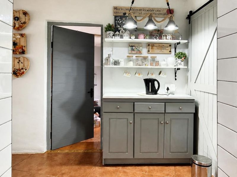A functional scullery area featuring built-in grey cabinetry, open shelving, and a sliding barn door, finished with tiled flooring and wall accents.