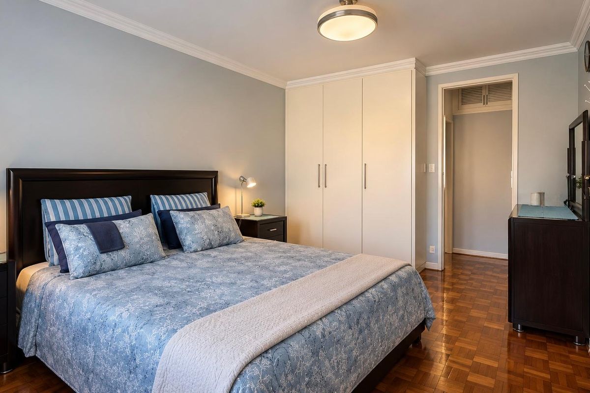 A well-maintained bedroom featuring classic parquet flooring, built-in cupboards, and elegant ceiling cornicing, offering a clean and comfortable living space.