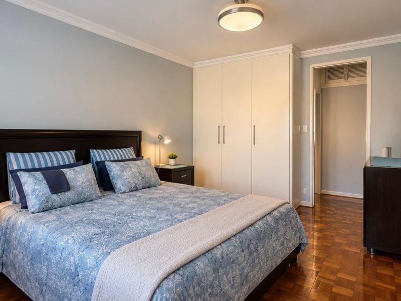 A well-maintained bedroom featuring classic parquet flooring, built-in cupboards, and elegant ceiling cornicing, offering a clean and comfortable living space.
