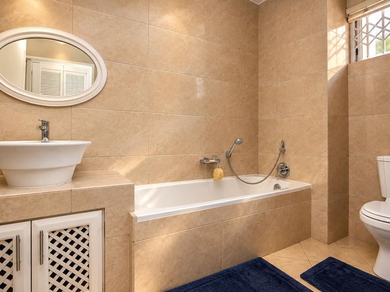 A well-maintained bathroom featuring floor-to-ceiling beige tiling, a built-in bathtub with shower mixer, a vessel sink vanity, and a toilet.