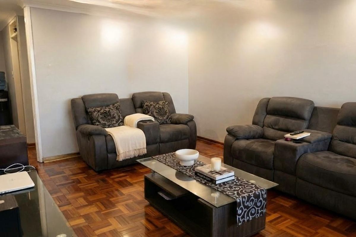 A comfortable living room featuring classic parquet flooring and recessed ceiling lighting, providing a warm and inviting atmosphere for relaxation.