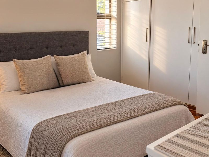 A well-maintained bedroom featuring built-in cupboards, parquet flooring, and natural light through venetian blinds.
