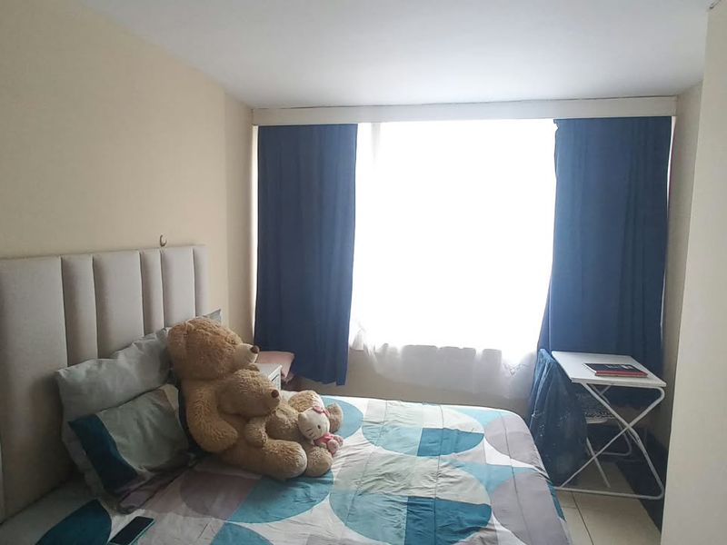 A standard bedroom featuring a large window with curtains and a wall-mounted light fixture.