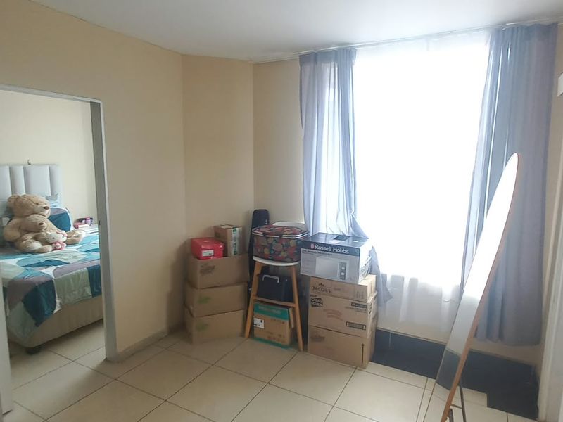A bedroom featuring tiled flooring, a sliding door, and a built-in cupboard, with a view into an adjacent bedroom space.