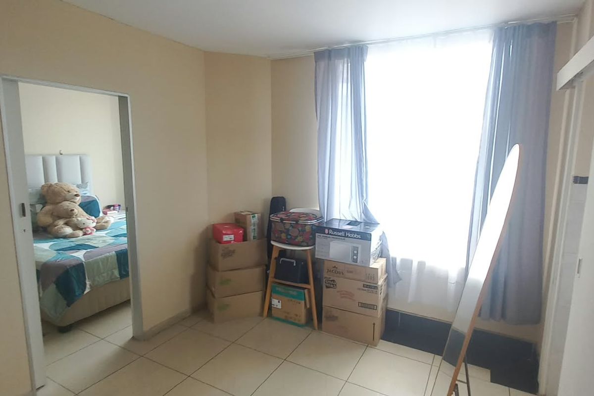 A bedroom featuring tiled flooring, a sliding door, and a built-in cupboard, with a view into an adjacent bedroom space.